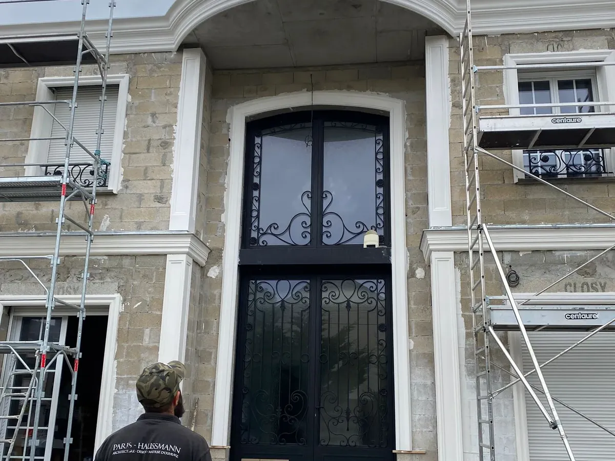 Artisan devant la façade en pierre d'un immeuble de style haussmannien, échafaudage en place