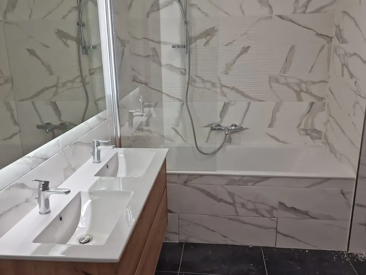 Salle de bain rénovée avec vasque double, grands carreaux marbrés et sol sombre