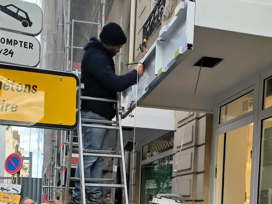 Artisan sur une échelle installant une enseigne en façade de commerce